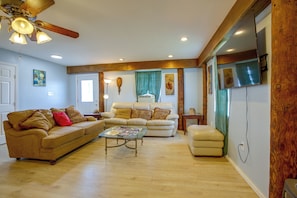A living room with a beige sofa, a glass coffee table, and a wooden ceiling fan. - Your Home Base in Southern Louisiana (Buras-Triumph)