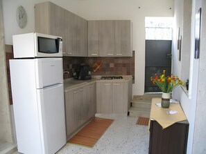 Et lille køkken med mikroovn, komfur og vask. Der er et ur på væggen og en vase med blomster på bordet.