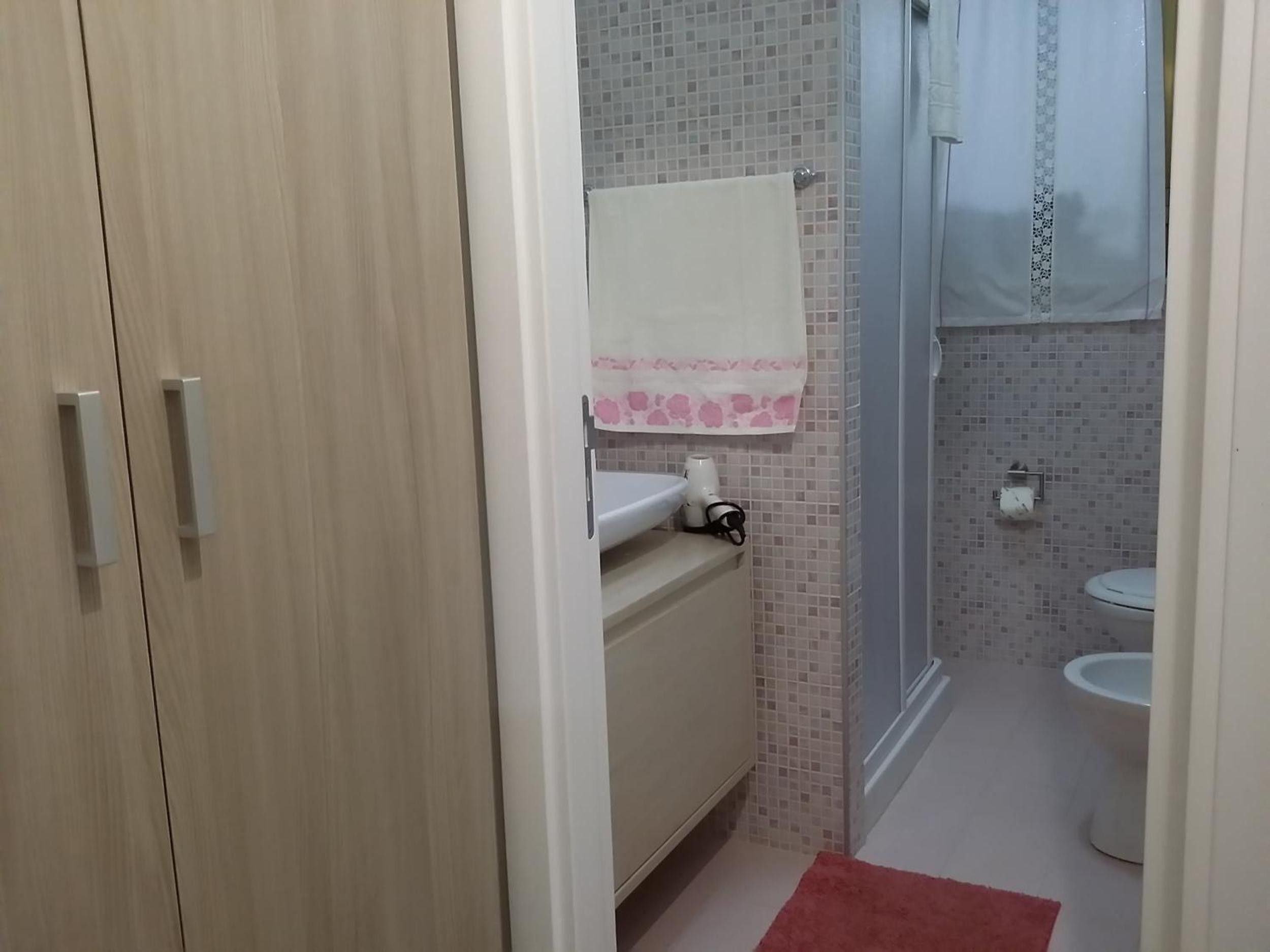 Een badkamer met toilet, wastafel, douche en een houten garderobe.
