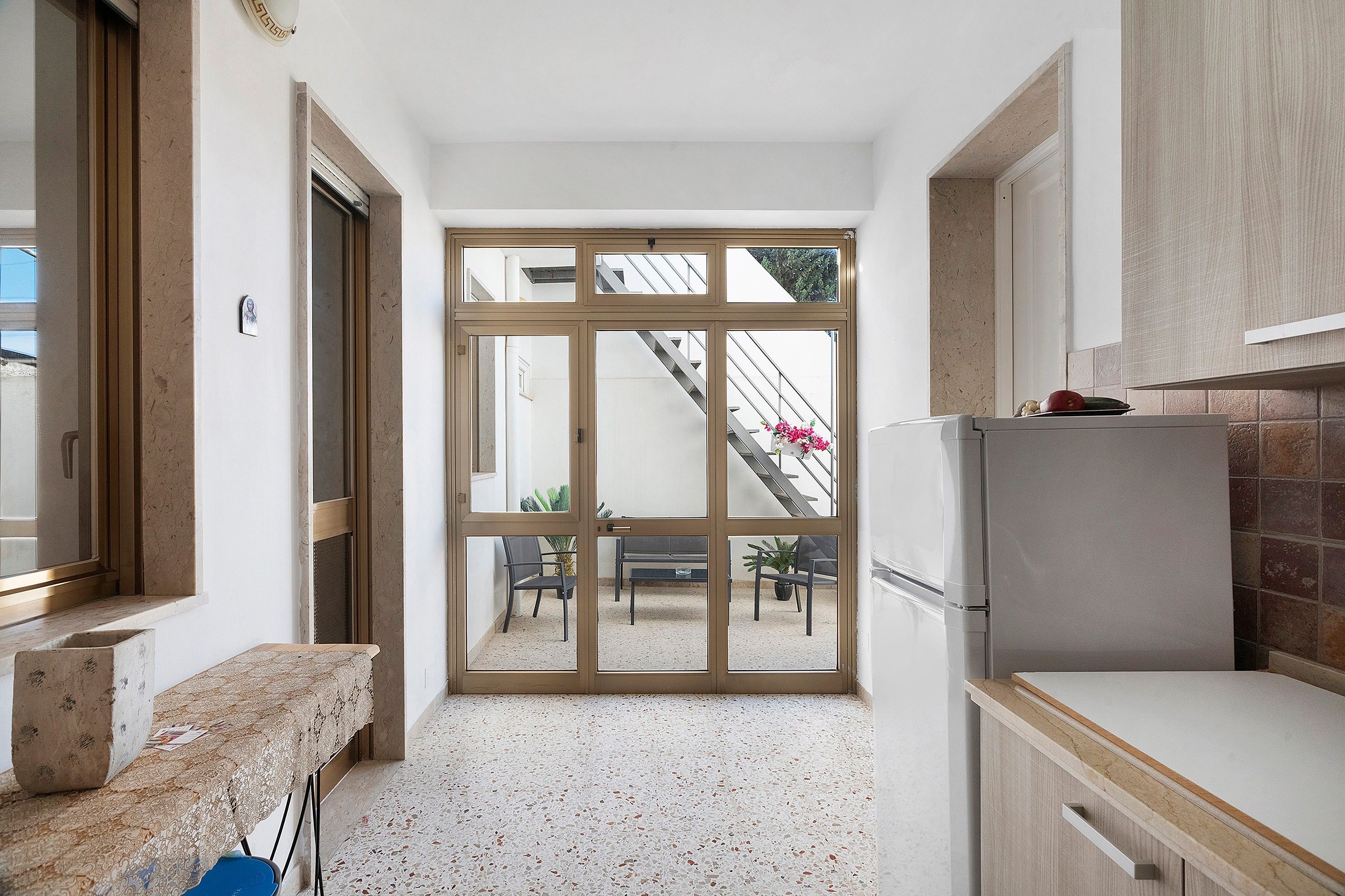 A compact kitchen with a built-in refrigerator, a bench, and a view of a staircase leading to an outdoor area.