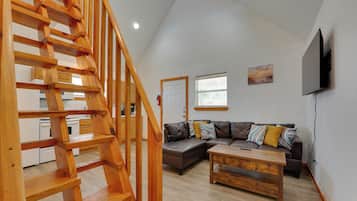Un interior moderno con una escalera de madera, un sofá modular, una mesa de centro y un televisor de pantalla plana montado en la pared.
