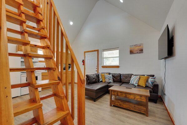A modern interior with a wooden staircase, a sectional sofa, a coffee table, and a flat-screen TV mounted on the wall.