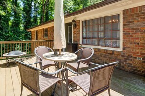 A covered patio with wicker furniture, a table, and a window overlooking a brick wall. - Atlanta Home w/ Deck, 18 Mi Outside Dtwn (Atlanta)