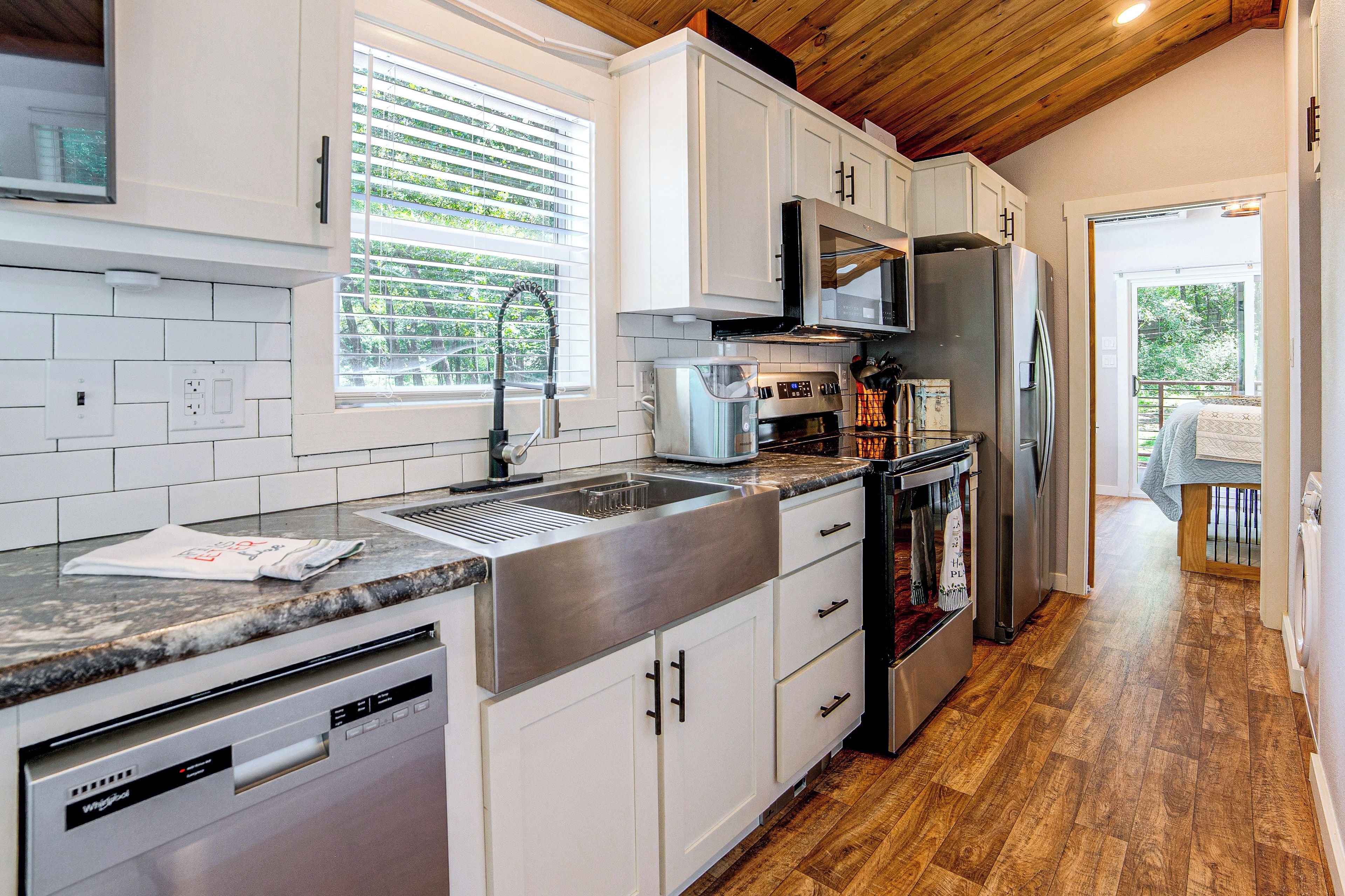 A modern kitchen with white cabinets, stainless steel appliances, and a wooden ceiling.