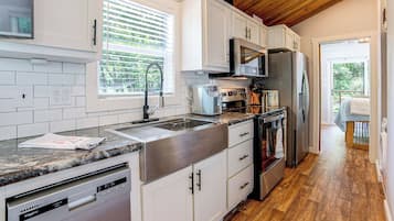 A modern kitchen with white cabinets, stainless steel appliances, and a wooden ceiling.