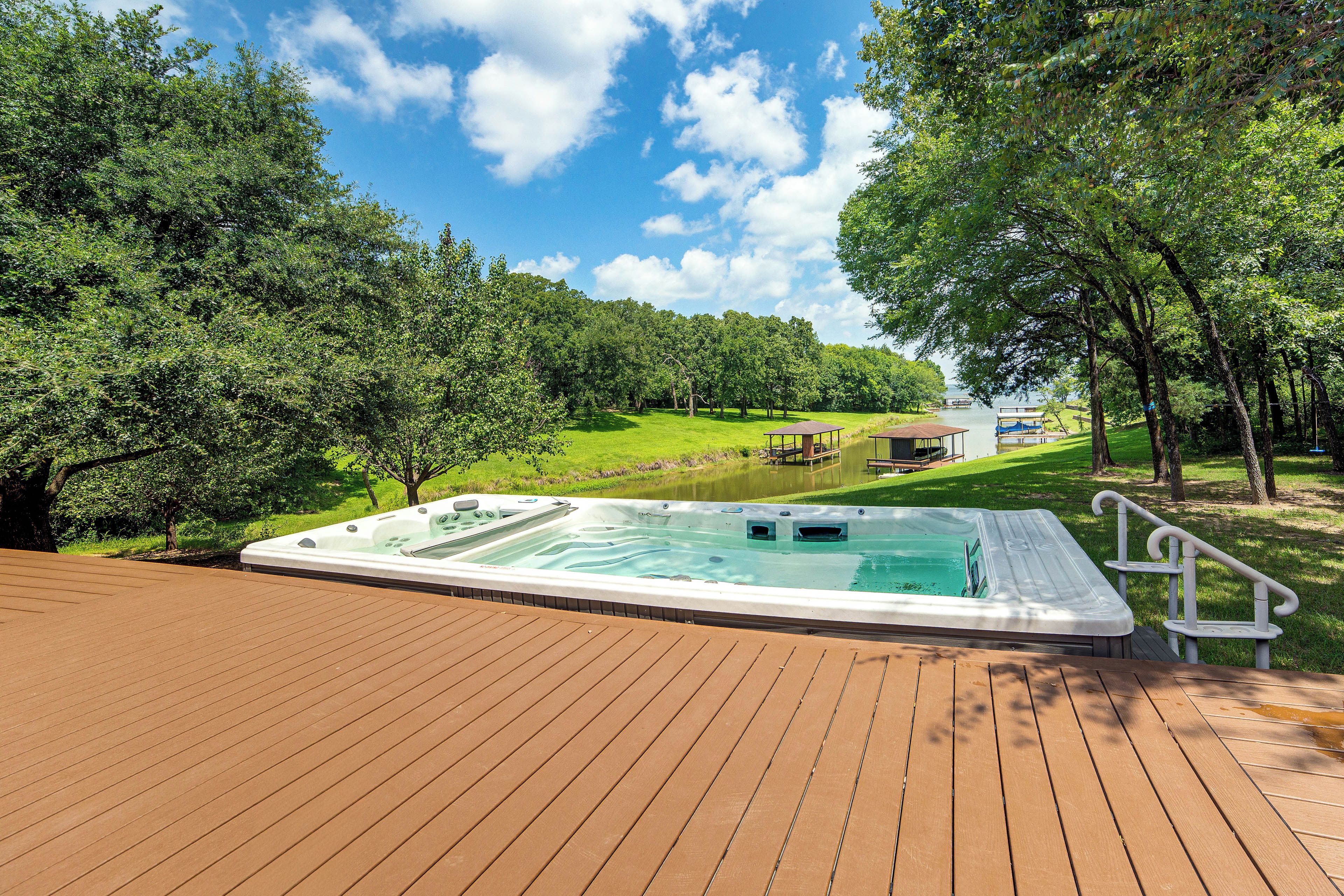 A hot tub on a wooden deck with a view of a lake and trees.