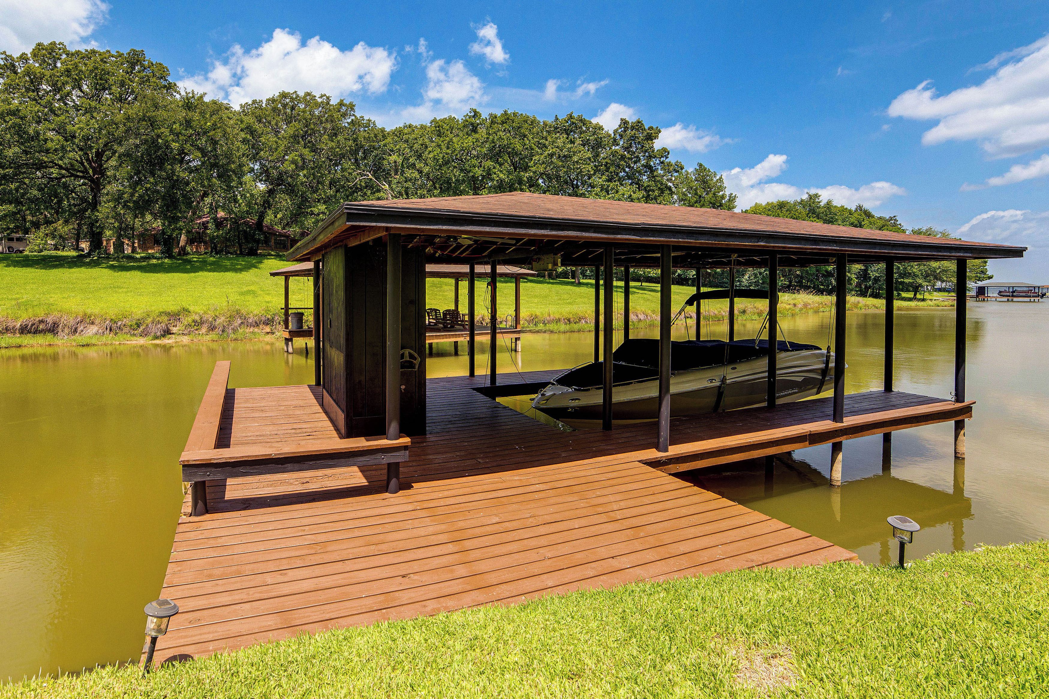 A wooden dock extending into a calm lake with a covered seating area and a boat docked on the right side.