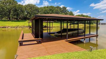 A wooden dock extending into a calm lake with a covered seating area and a boat docked on the right side.