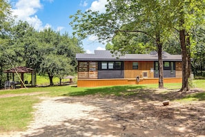 A cabin with a deck, surrounded by trees and a clear sky.