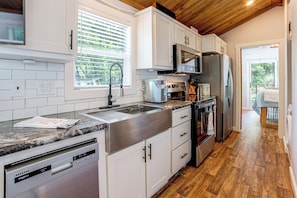 A modern kitchen with white cabinets, stainless steel appliances, and a wooden ceiling.