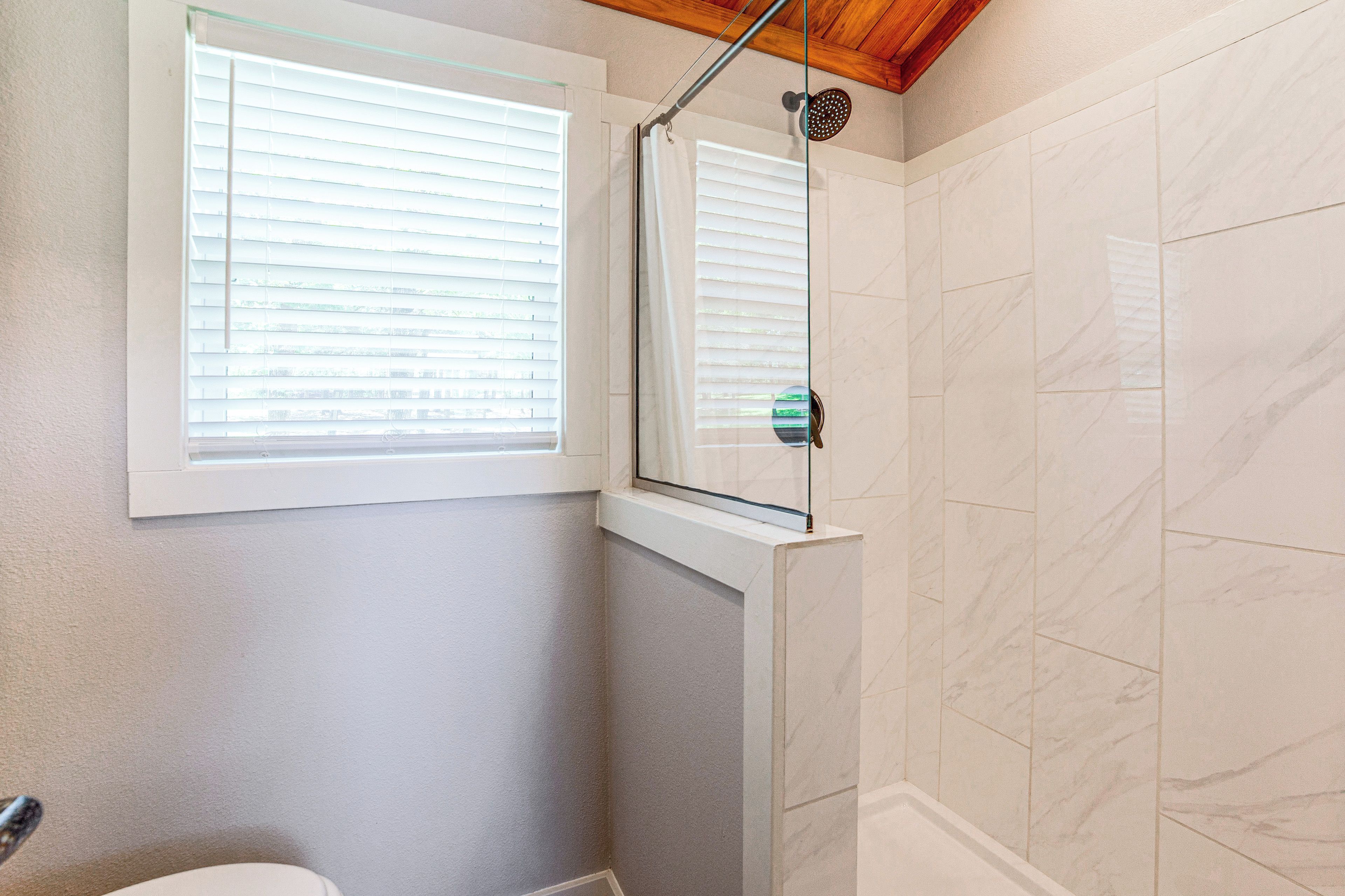 A bathroom with a shower, a toilet, and a window.