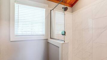 A bathroom with a shower, a toilet, and a window.