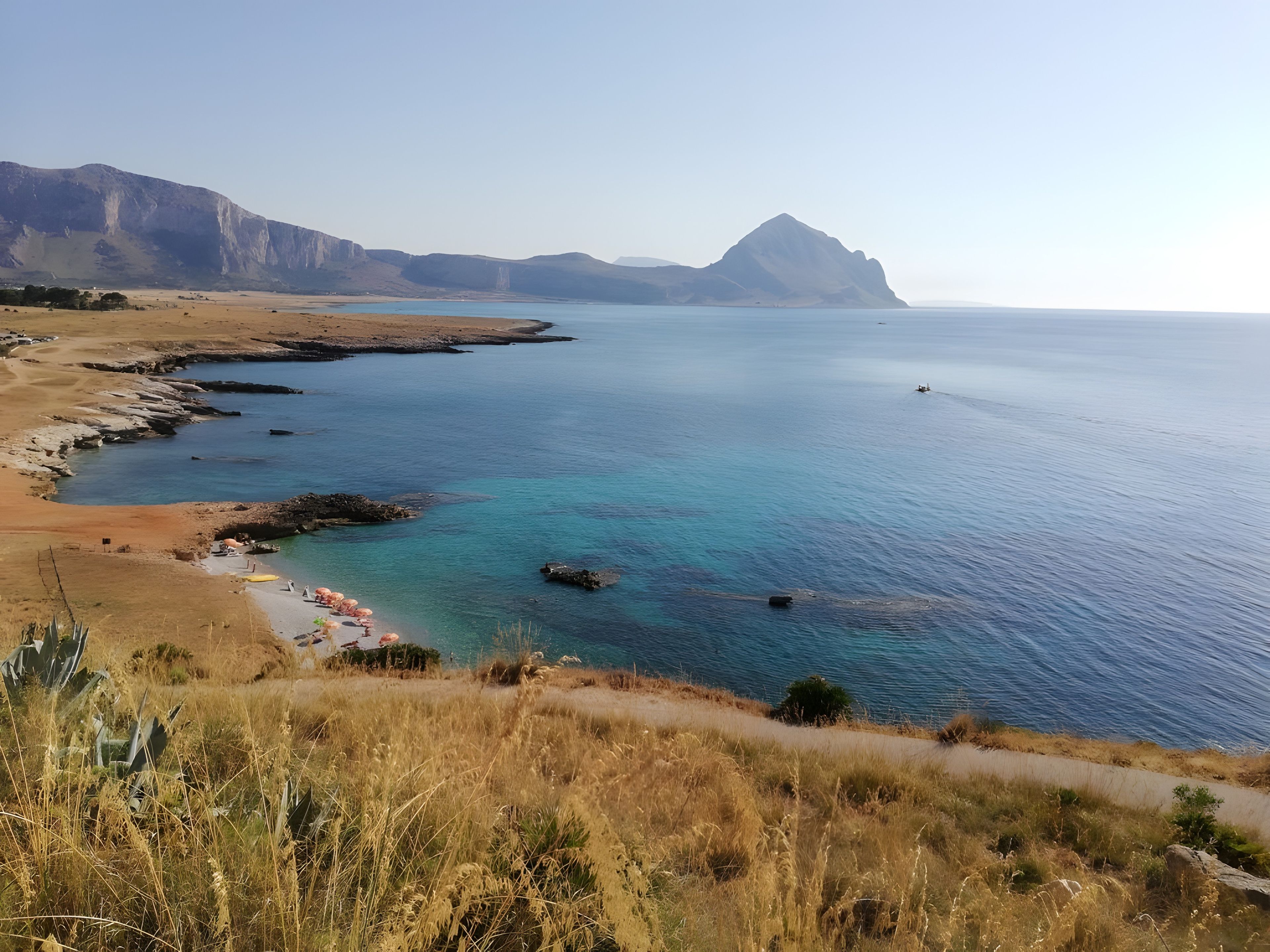 Un paisaje costero con vista despejada al mar, una playa de arena y montañas distantes.