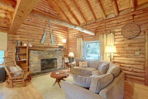 A log cabin interior with a stone fireplace, wooden furniture, and a large clock on the wall. - Waterfront Log Cabin w/ Fire Pit in Mayville! (Mayville)