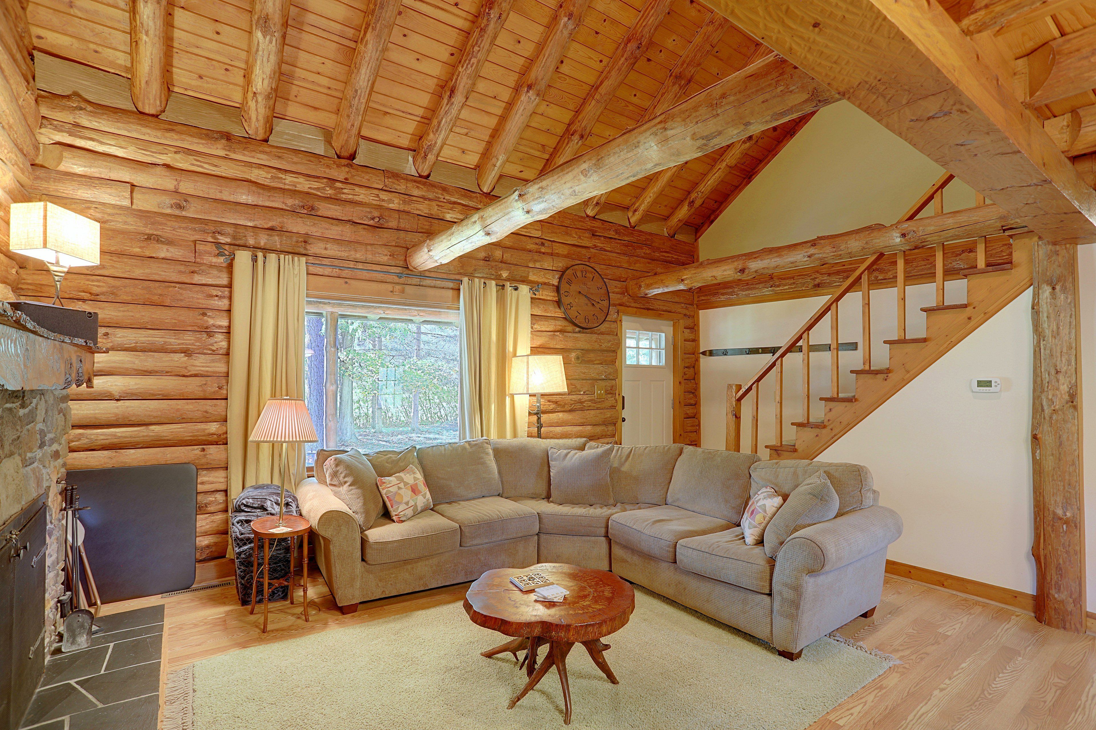 A log cabin interior with a wooden staircase, a sectional sofa, a small round table, and a fireplace.
