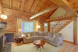 A log cabin interior with a wooden staircase, a sectional sofa, a small round table, and a fireplace.