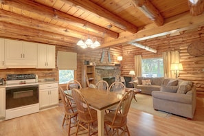 A log cabin interior with a dining area, kitchen, and living space.