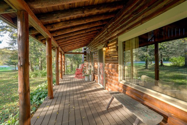 A wooden deck with a covered area, large windows, and a view of a natural landscape.