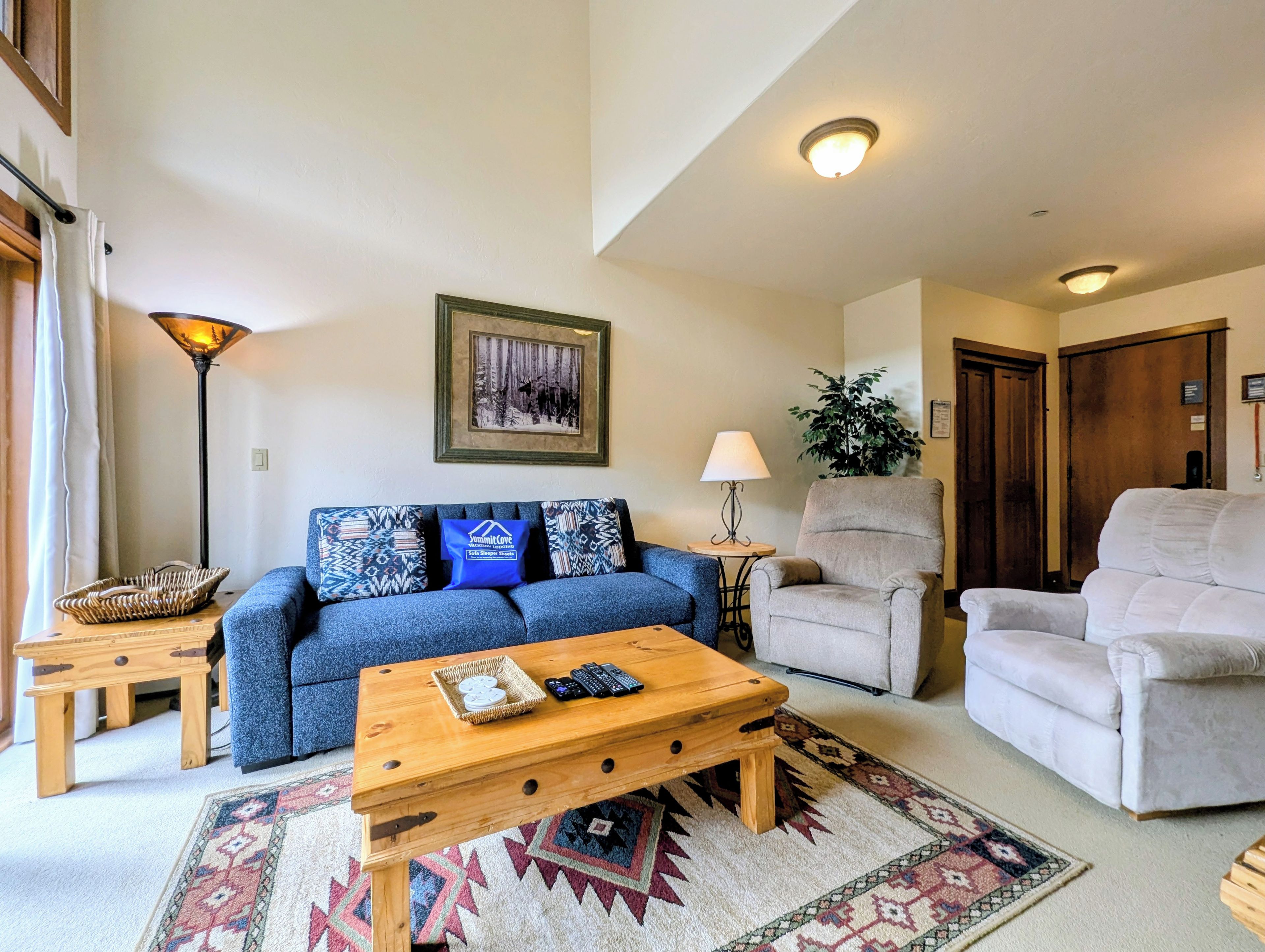 A living room with a blue sofa, a wooden coffee table, a beige armchair, a patterned rug, and a framed picture on the wall.
