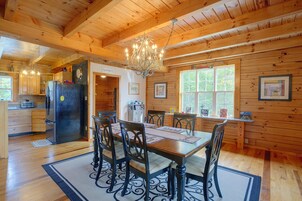 A wooden interior with a dining table, chairs, a chandelier, and a kitchen area.