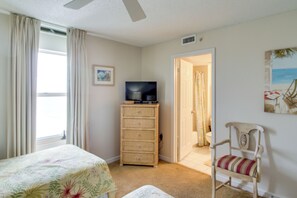A bedroom with a bed, a chair, a television on a dresser, and a door leading to a bathroom. - Steps to Beach 18th-floor Condo, 3 Pools in Destin (Destin)