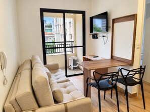 A modern living room with a sofa, a dining table with chairs, a TV mounted on the wall, and a balcony with a view of buildings. - New Listing (São Paulo)