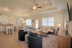 A spacious living room with a ceiling fan, a kitchen area with white cabinets, and a dining space with a table and chairs. - Stunning Murrells Inlet Townhome Near Marshwalk (Murrells Inlet)