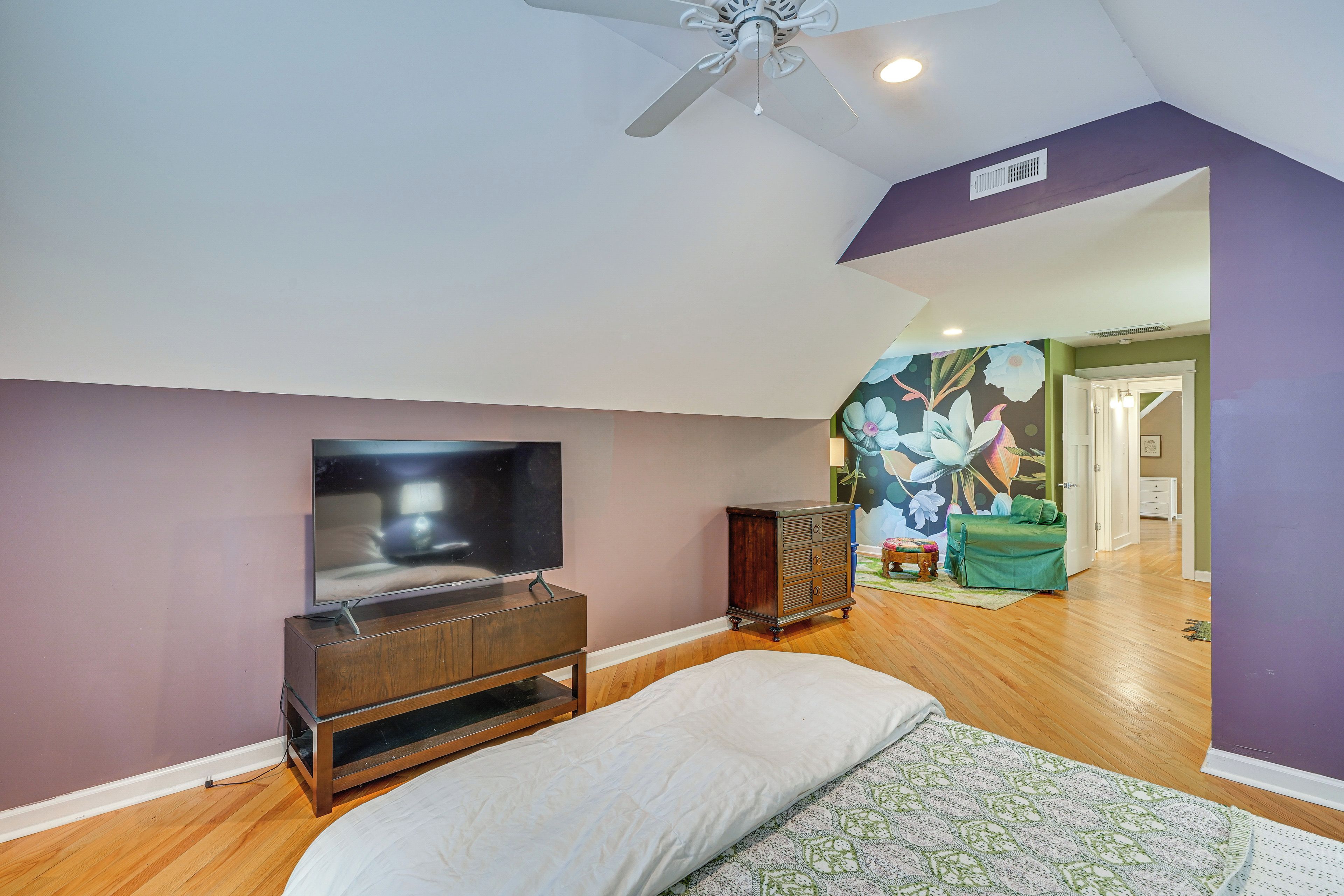 A bedroom with a bed, a TV, a dresser, and a ceiling fan.