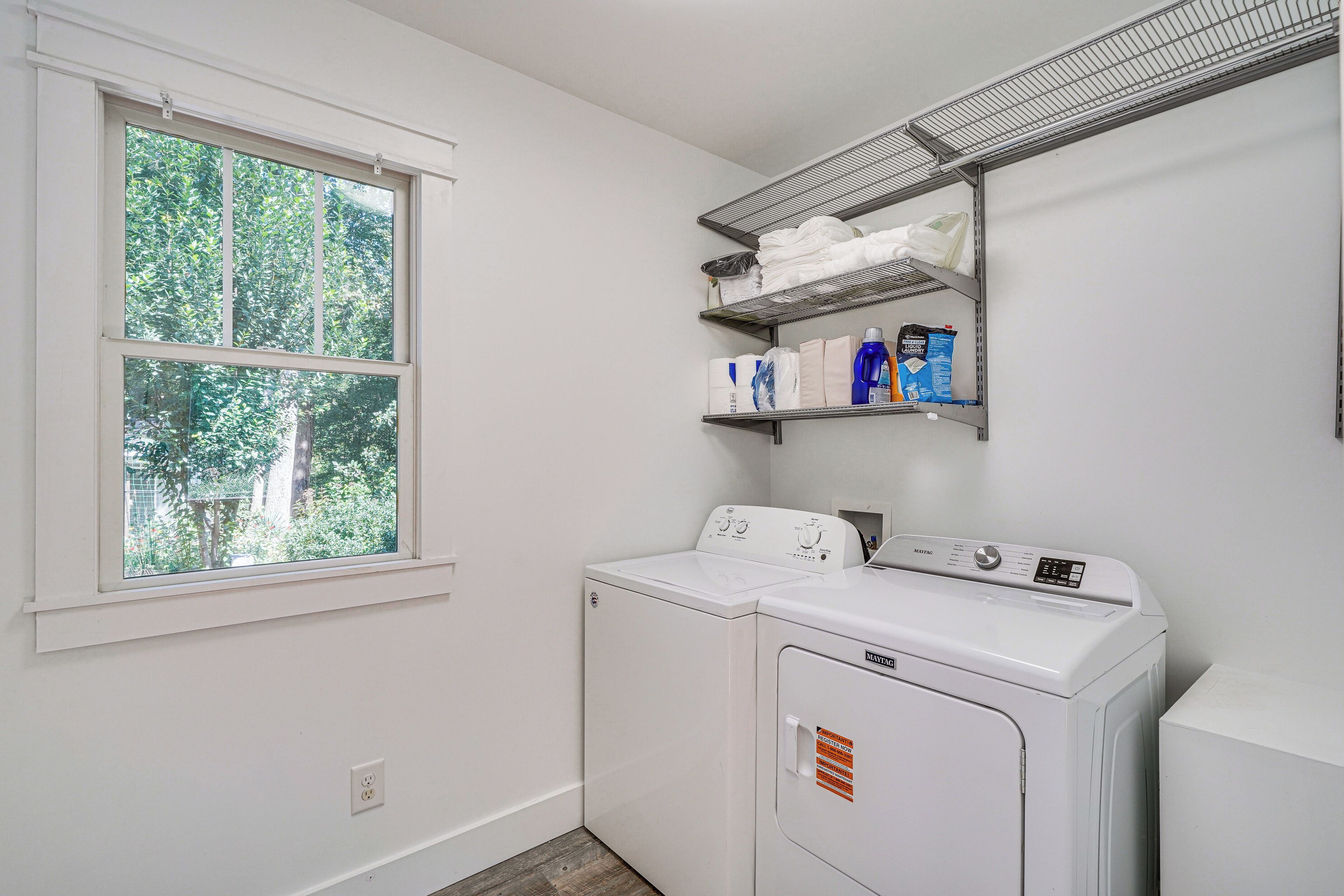 A laundry room with a washing machine, a dryer, a window, and shelves with laundry supplies.