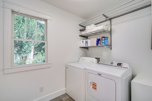 A laundry room with a washing machine, a dryer, a window, and shelves with laundry supplies. - Deck & Yard! Tri-city Family Home Near UNC & Duke (Chapel Hill)