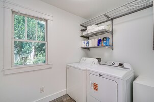 Un lavadero con lavadora, secadora, una ventana y estantes con productos de limpieza.