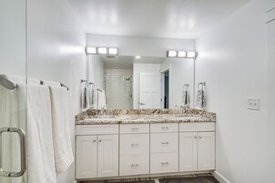 Un baño con un espejo grande, dos lavamanos, una ducha y un perchero para toallas.