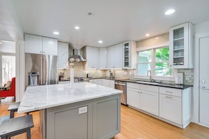 Cocina moderna con armarios blancos, una isla de mármol, electrodomésticos de acero inoxidable y una ventana con vistas a zonas verdes.