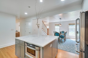 A modern kitchen with a central island, stainless steel appliances, and a dining area with blue chairs. - Deck & Yard! Tri-city Family Home Near UNC & Duke (Chapel Hill)
