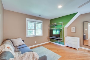 Una sala de estar con un sofá, un televisor de pantalla plana sobre un mueble, una pared de acento verde y una escalera.