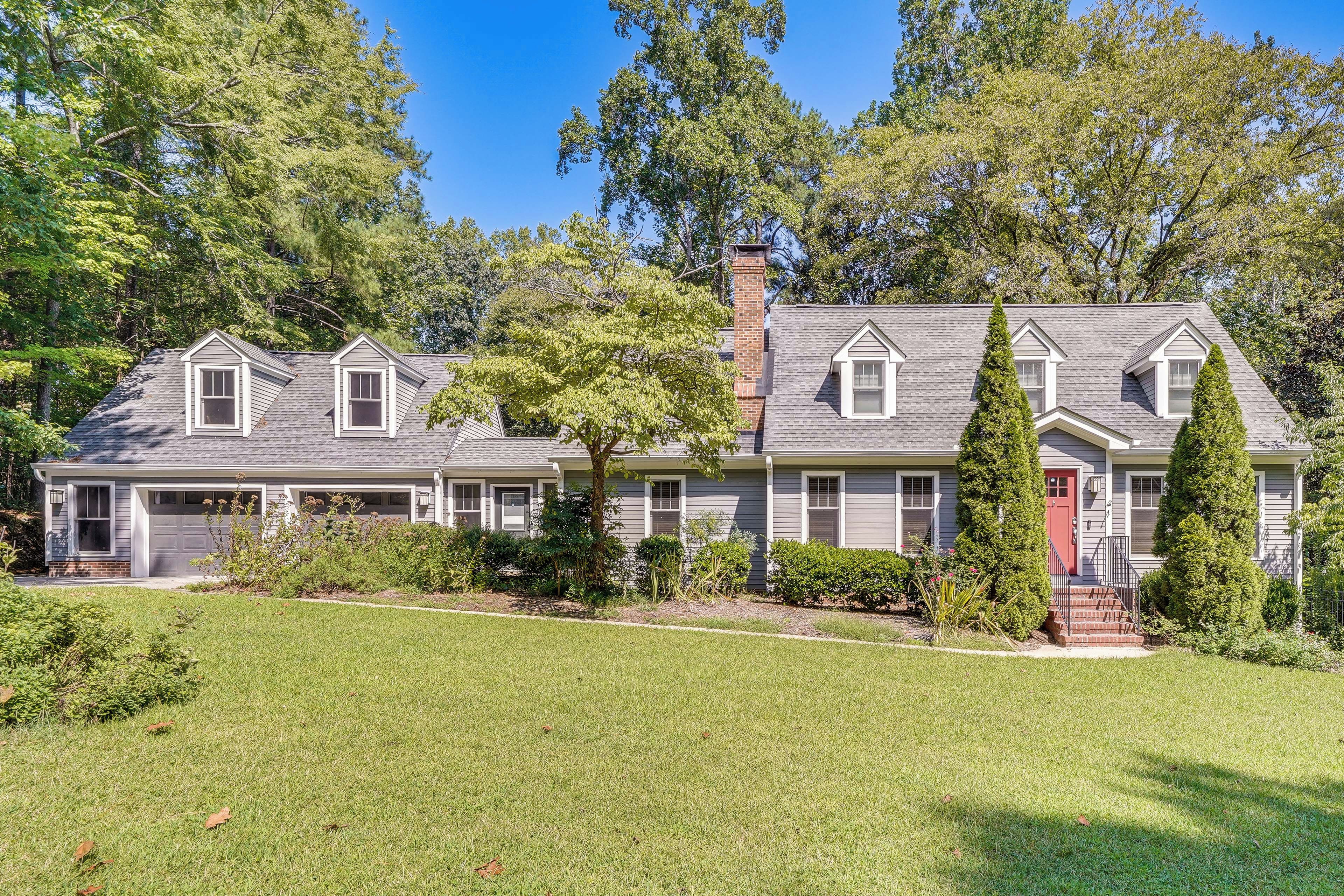 A two-story house with a garage, a red door, and a well-maintained lawn.