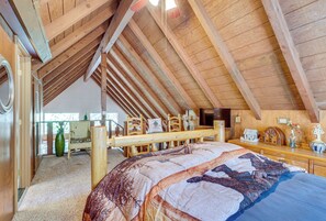 Ein Zimmer mit hohen Decken, einer Holzbodenverkleidung, einem Bett mit gemustertem Überwurf, einem Fernseher und einem kleinen Tisch mit Dekoration.
