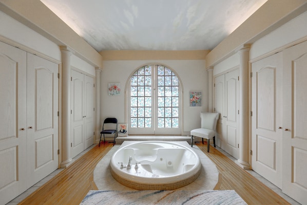 A spacious bathroom with a freestanding bathtub, a large arched window, and a white tiled floor.