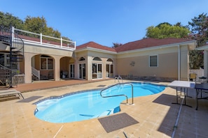 Una propiedad residencial con piscina, un patio cubierto y una casa de dos pisos con balcón.