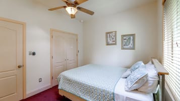 A bedroom with a bed, a ceiling fan, a door, and two framed pictures on the wall.
