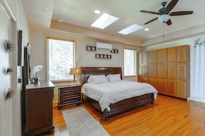 A bedroom with a wooden bed, a nightstand, a dresser, a ceiling fan, and a large window with blinds.