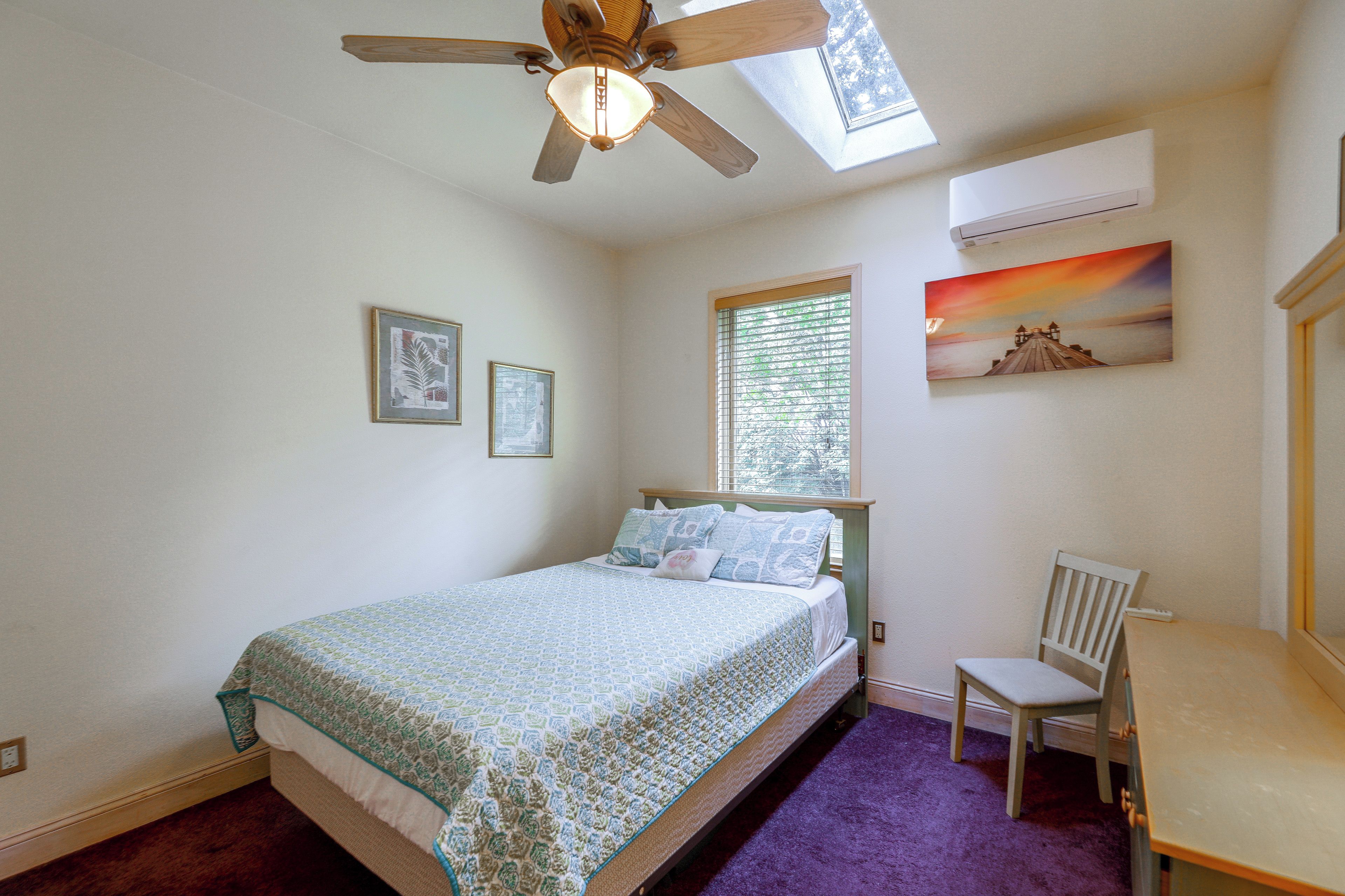 Une chambre à coucher avec un lit, une chaise, un ventilateur de plafond, une fenêtre avec des stores et un tableau au mur.