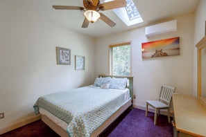 Un dormitorio con cama, una silla, ventilador de techo, ventana con persianas y un cuadro en la pared.