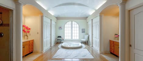A spacious hallway with wooden flooring, a central seating area, and a large arched window.