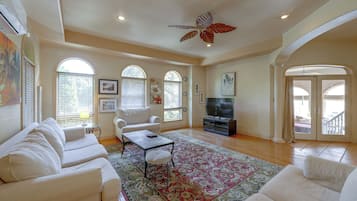 A spacious living room with a large sofa set, a coffee table, a television, and a decorative ceiling fan.