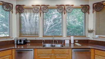 A kitchen with a built-in dishwasher, a double sink, and a window with blinds.