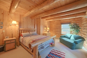 Ein Schlafzimmer in einer Blockhütte mit einem Bett, Nachttischen, einem Schminktisch, einem Stuhl und einem Fenster.