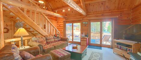 A log cabin interior with a sofa, ottoman, table, and a television.