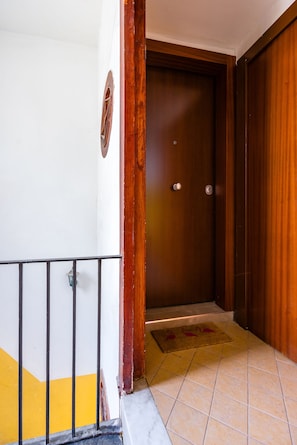 A wooden door with a metal handle, a small circular window, and a tiled floor with a yellow and white pattern. - Rega 37 (Naples)