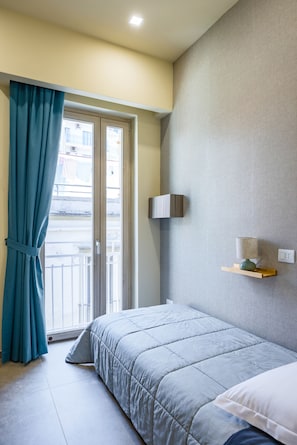 Ein Schlafzimmer mit Bett, einem fenster mit Vorhängen, einem an der Wand befestigten Regal und einer Tür, die auf einen Balkon führt.